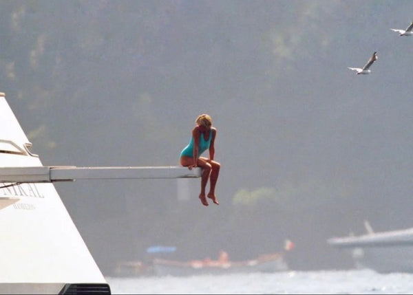 Princess Diana in a turquoise swimsuit sitting on a diving board over the sea, timeless swimwear icon