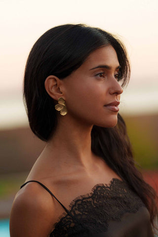Woman with long dark hair wearing gold earrings against a blurred natural background